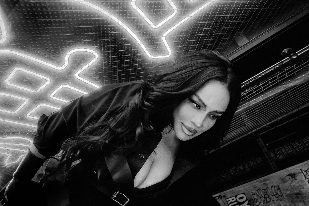 Black haired latin woman in a leather outfit standing in front of a neon sign in kanji in tokyo